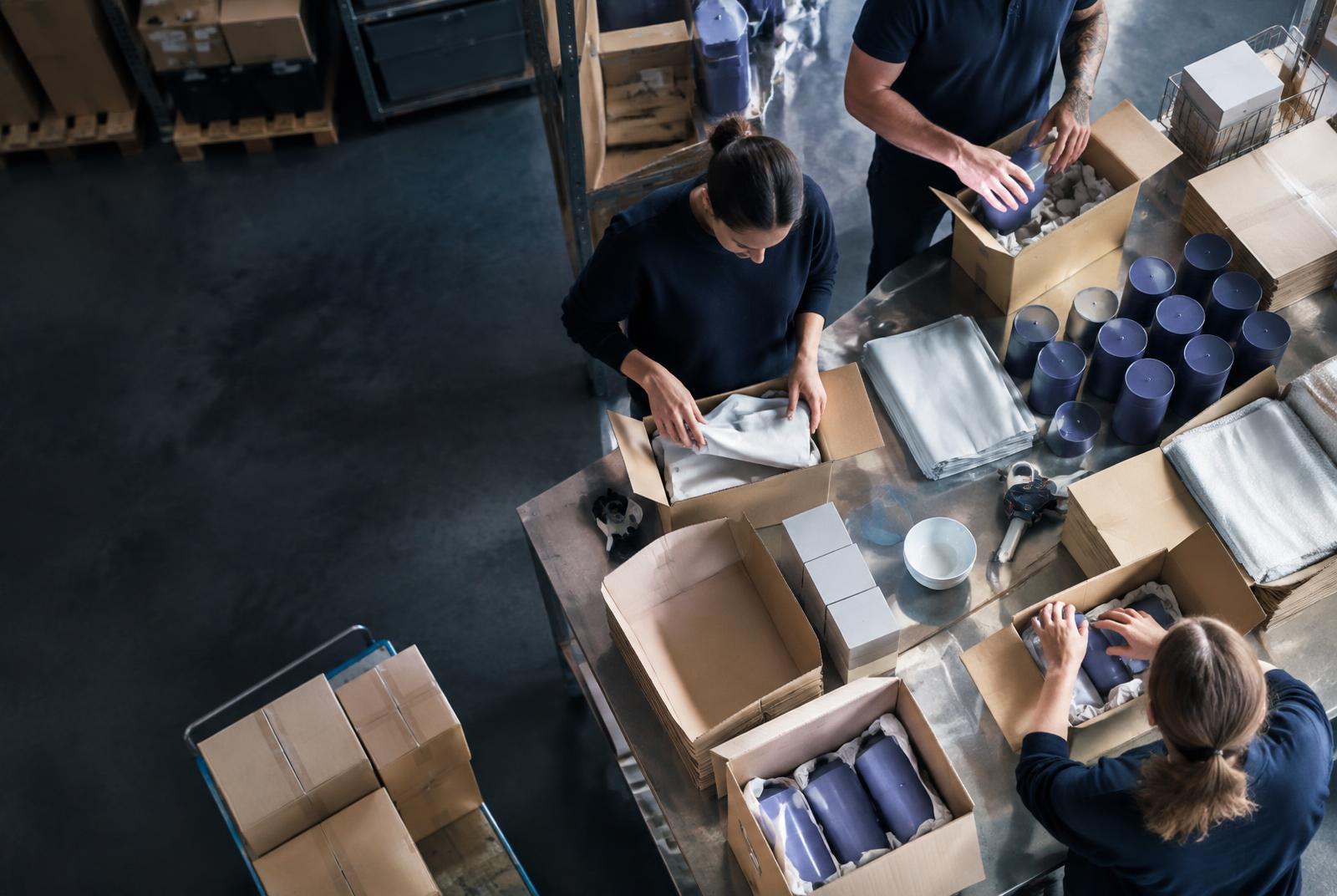 Mehrere Personen packen Waren an einem großen Arbeitstisch in neue Verpackungen um